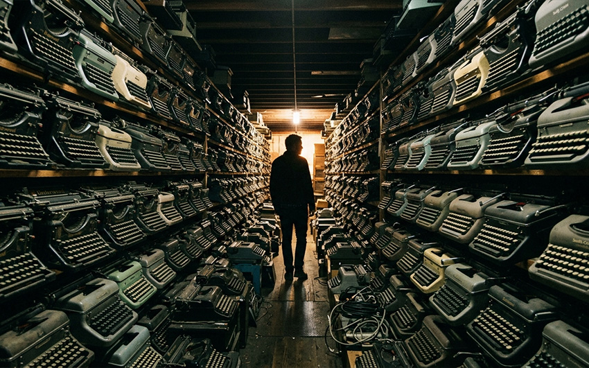 A figure walking among his typewriter collection